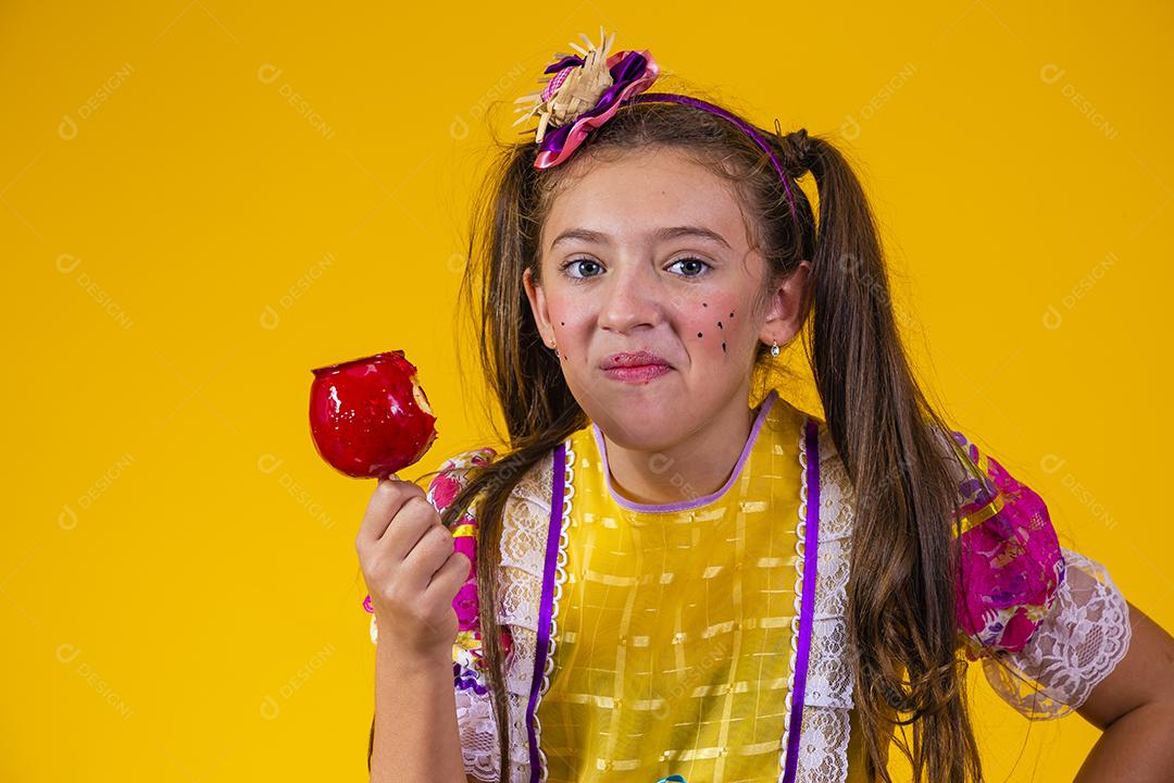 Linda garota caucasiana com roupa típica de festa junina comendo maçã com caramelo.