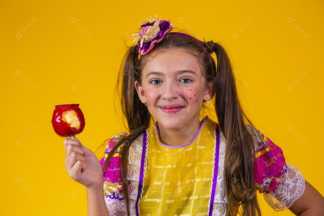 Linda garota caucasiana com roupa típica de festa junina comendo maçã com caramelo.