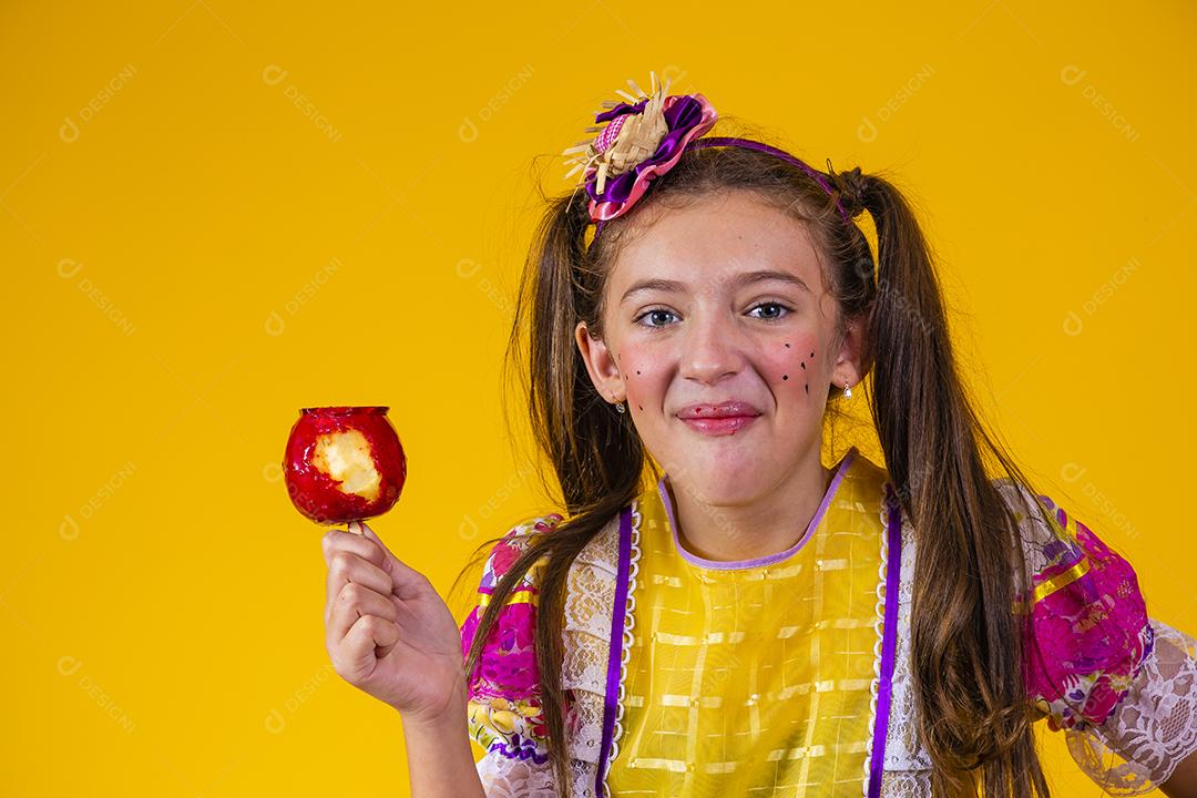 Linda garota caucasiana com roupa típica de festa junina comendo maçã com caramelo.