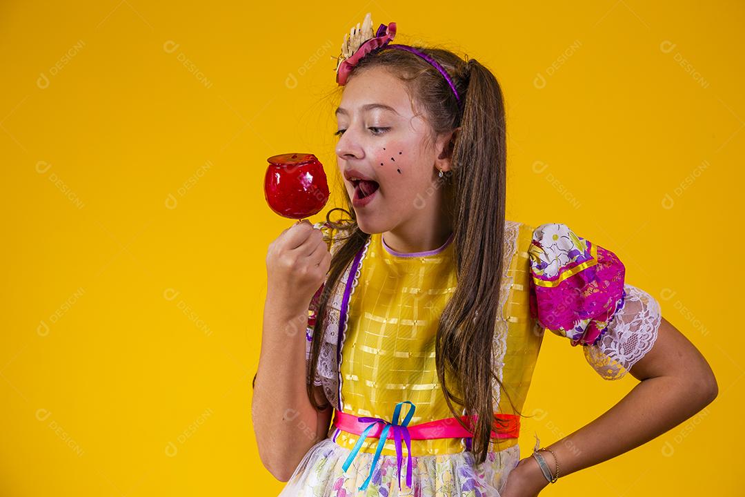 Linda garota caucasiana com roupa típica de festa junina comendo maçã com caramelo.