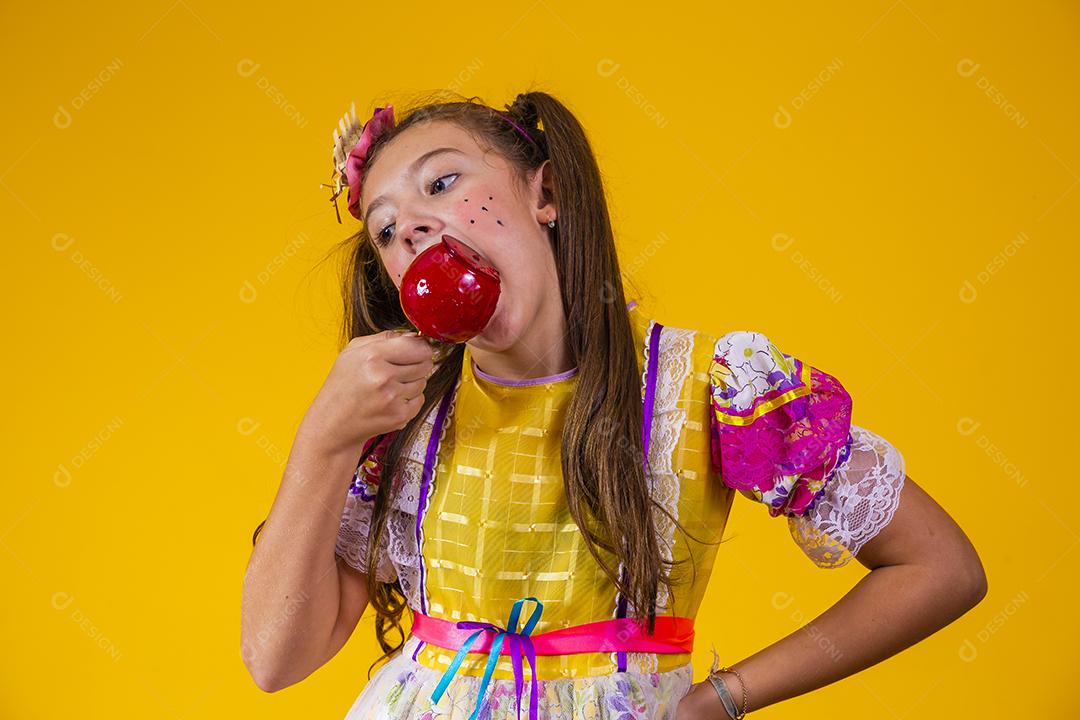 Linda garota caucasiana com roupa típica de festa junina comendo maçã com caramelo.