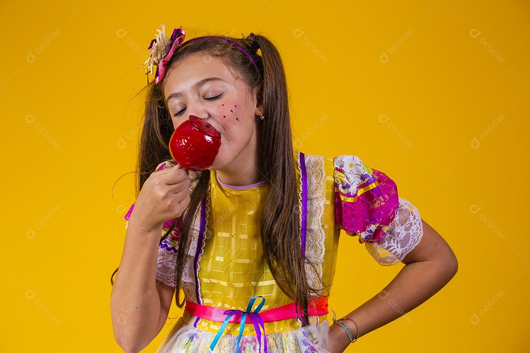 Linda garota caucasiana com roupa típica de festa junina comendo maçã com caramelo.