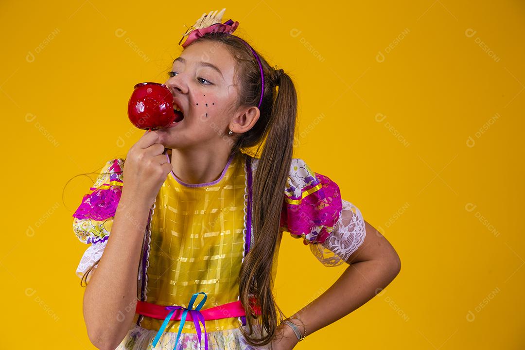 Linda garota caucasiana com roupa típica de festa junina comendo maçã com caramelo.