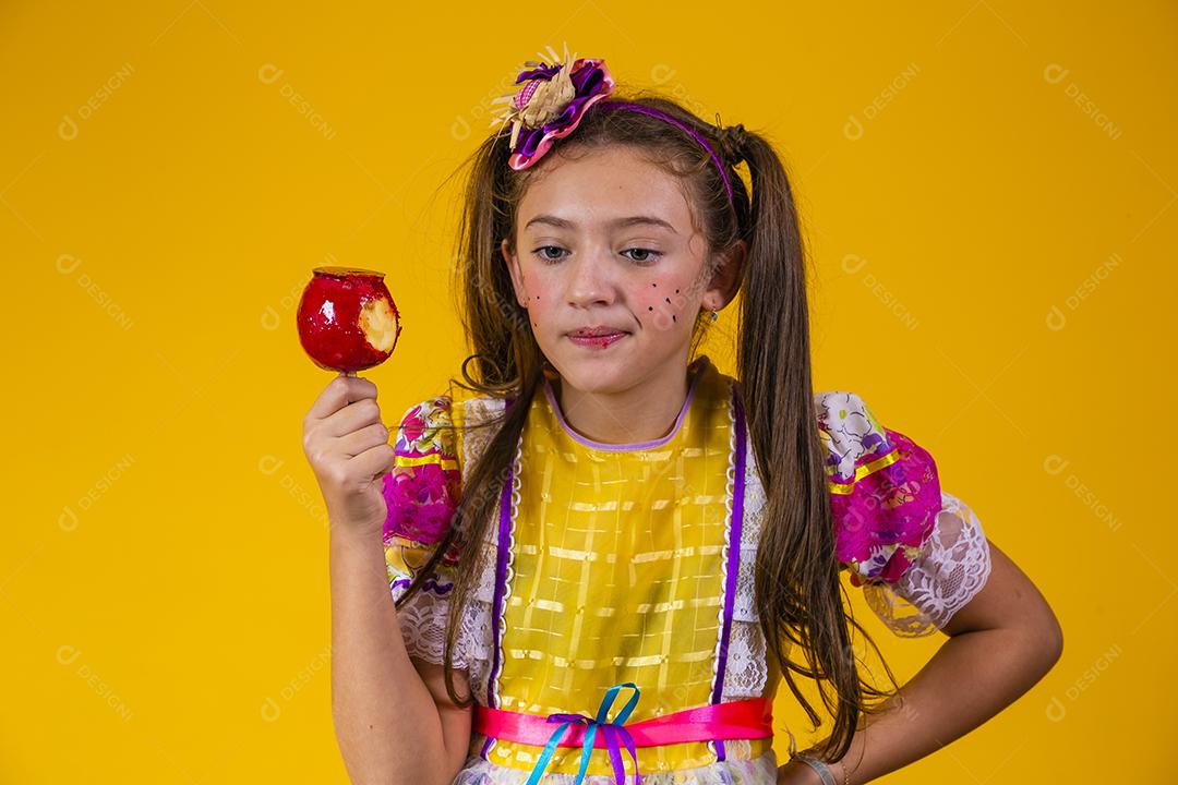 Linda garota caucasiana com roupa típica de festa junina comendo maçã com caramelo.