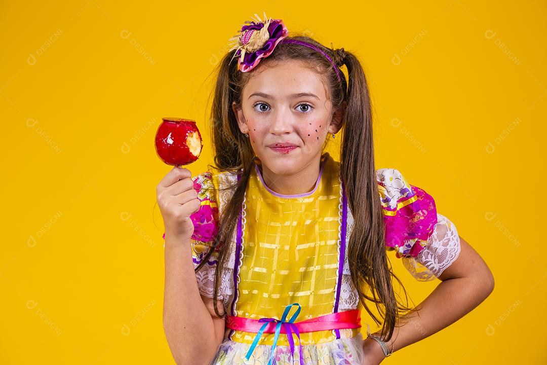Linda garota caucasiana com roupa típica de festa junina comendo maçã com caramelo.