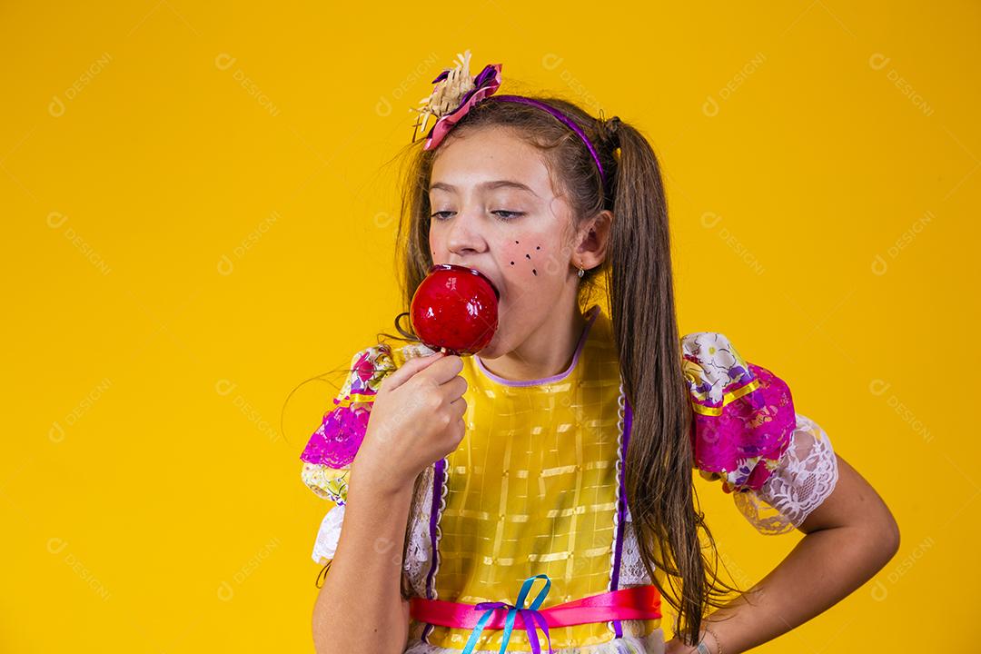 Linda garota caucasiana com roupa típica de festa junina comendo maçã com caramelo.