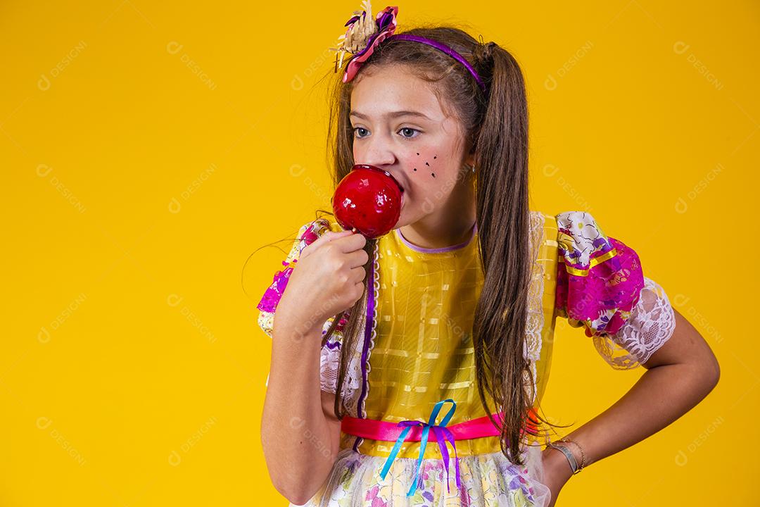 Linda garota caucasiana com roupa típica de festa junina comendo maçã com caramelo.