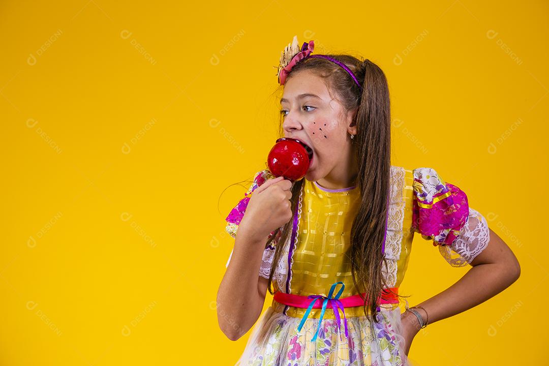 Linda garota caucasiana com roupa típica de festa junina comendo maçã com caramelo.