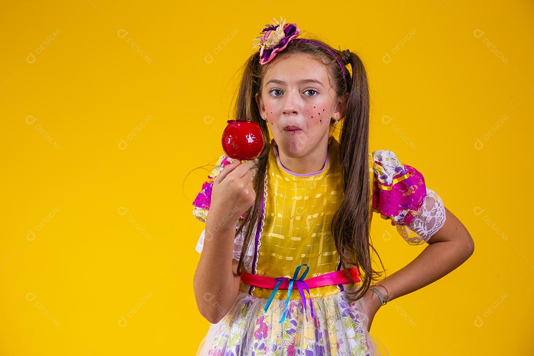 Linda garota caucasiana com roupa típica de festa junina comendo maçã com caramelo.