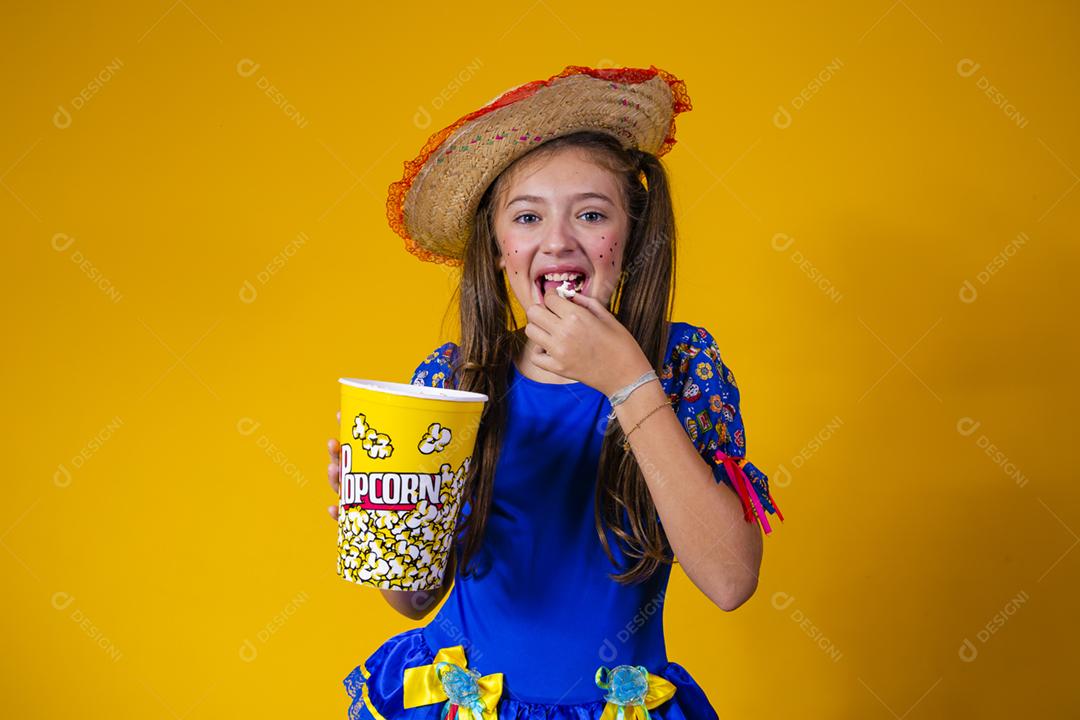 Menina caucasiana bonitinha com roupa típica de festa junina comendo