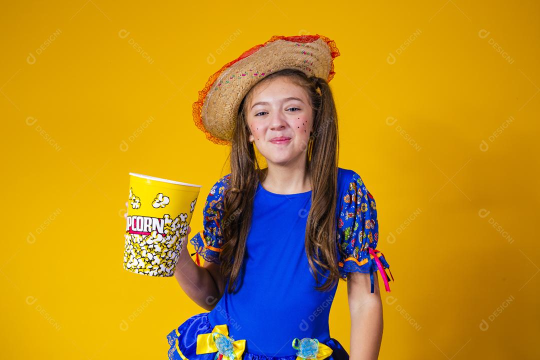 Menina caucasiana bonitinha com roupa típica de festa junina comendo