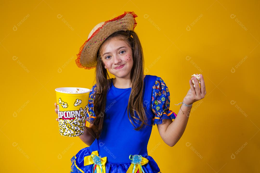 Menina caucasiana bonitinha com roupa típica de festa junina comendo