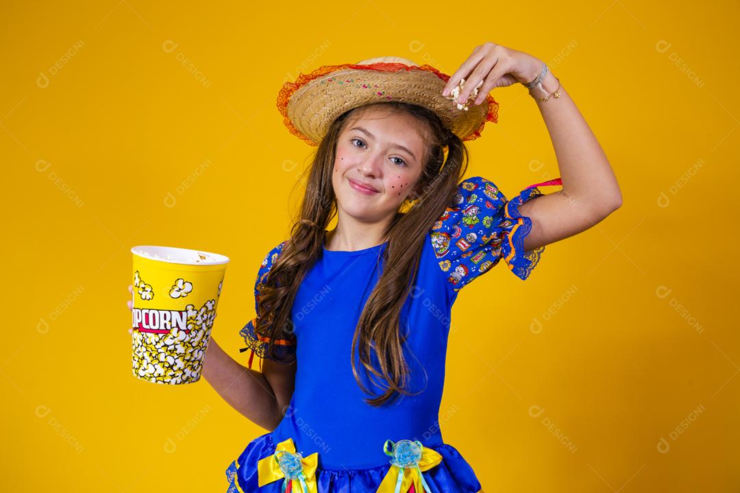 Menina caucasiana bonitinha com roupa típica de festa junina comendo