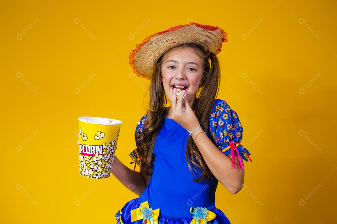 Menina caucasiana bonitinha com roupa típica de festa junina comendo