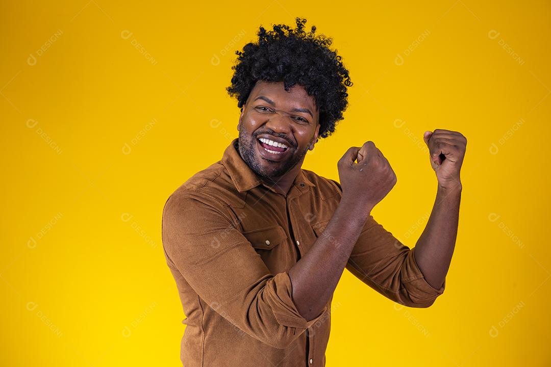 Homem afro comemorando grande sorte e sucesso olhando para câmera posando no estúdio sobre fundo amarelo