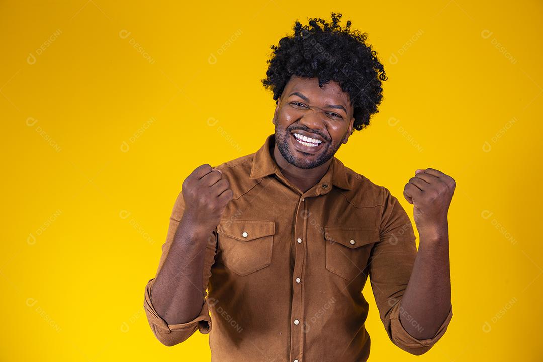 Homem afro comemorando grande sorte e sucesso olhando para câmera posando no estúdio sobre fundo amarelo