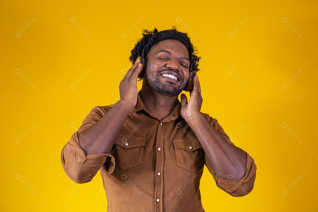Homem Africano feliz sorrindo ouvindo música em fones de ouvido. Fundo amarelo.