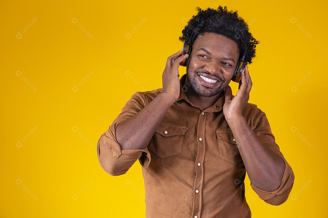 Homem Africano feliz sorrindo ouvindo música em fones de ouvido. Fundo amarelo.