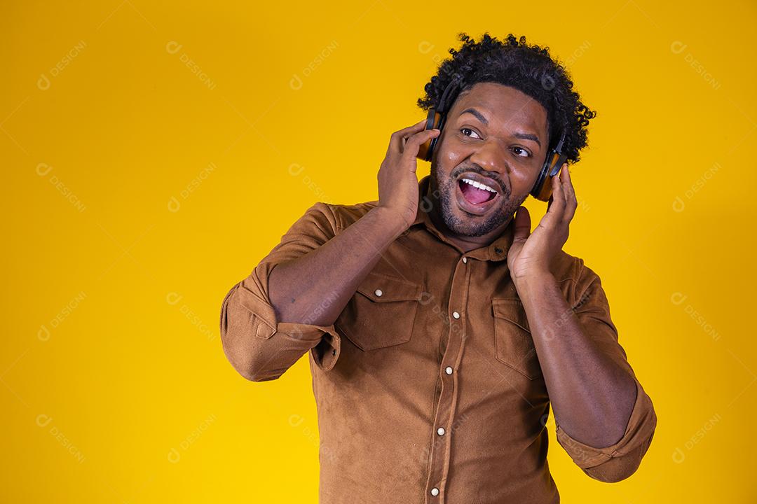 Homem Africano feliz sorrindo ouvindo música em fones de ouvido. Fundo amarelo.