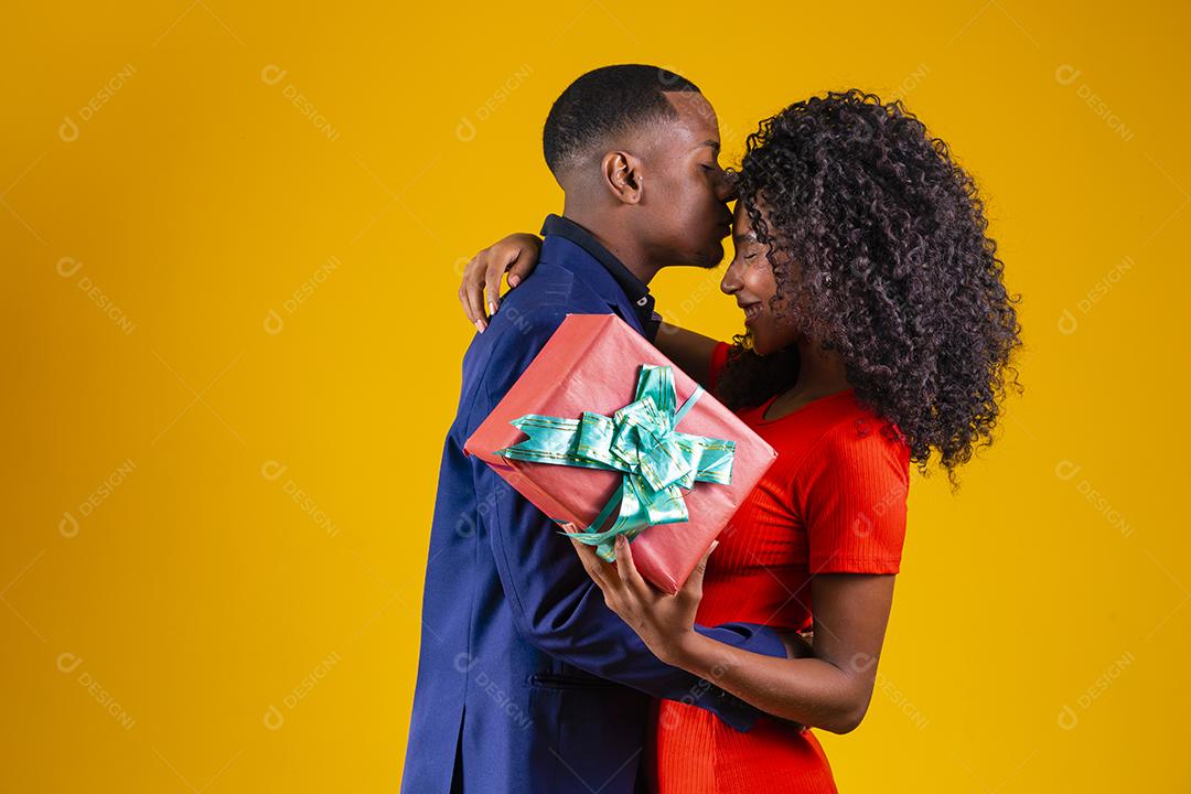 Retrato de um lindo casal afro em fundo amarelo segurando um presente