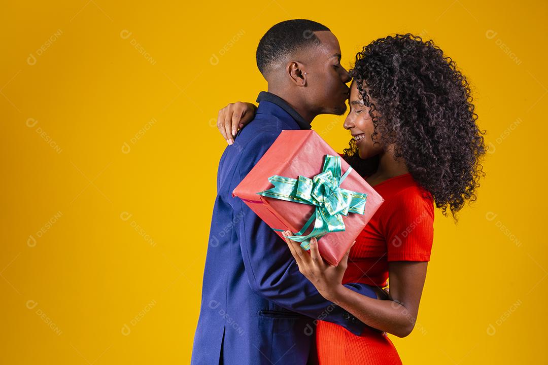 Retrato de um lindo casal afro em fundo amarelo segurando um presente