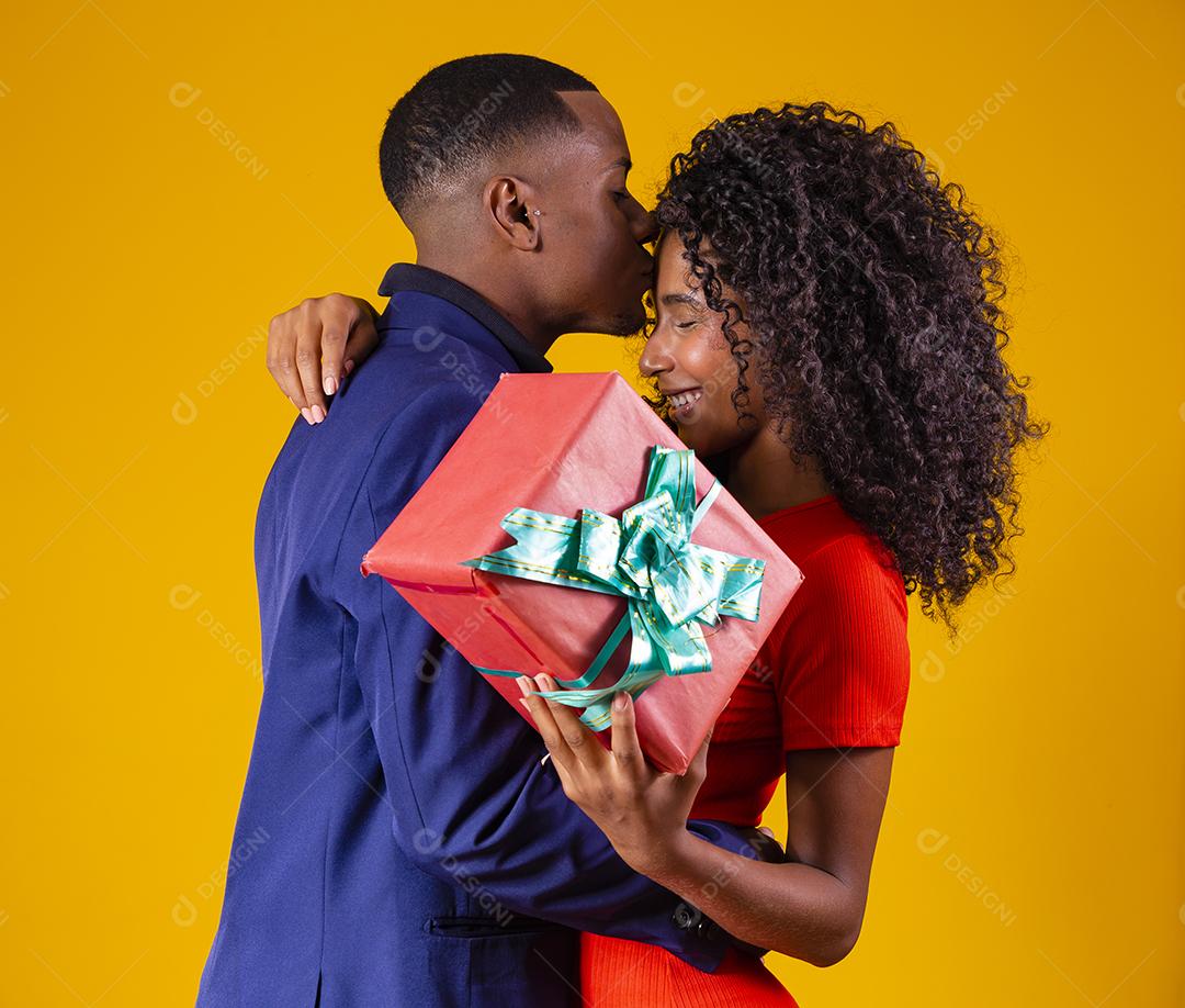 Retrato de um lindo casal afro em fundo amarelo segurando um presente
