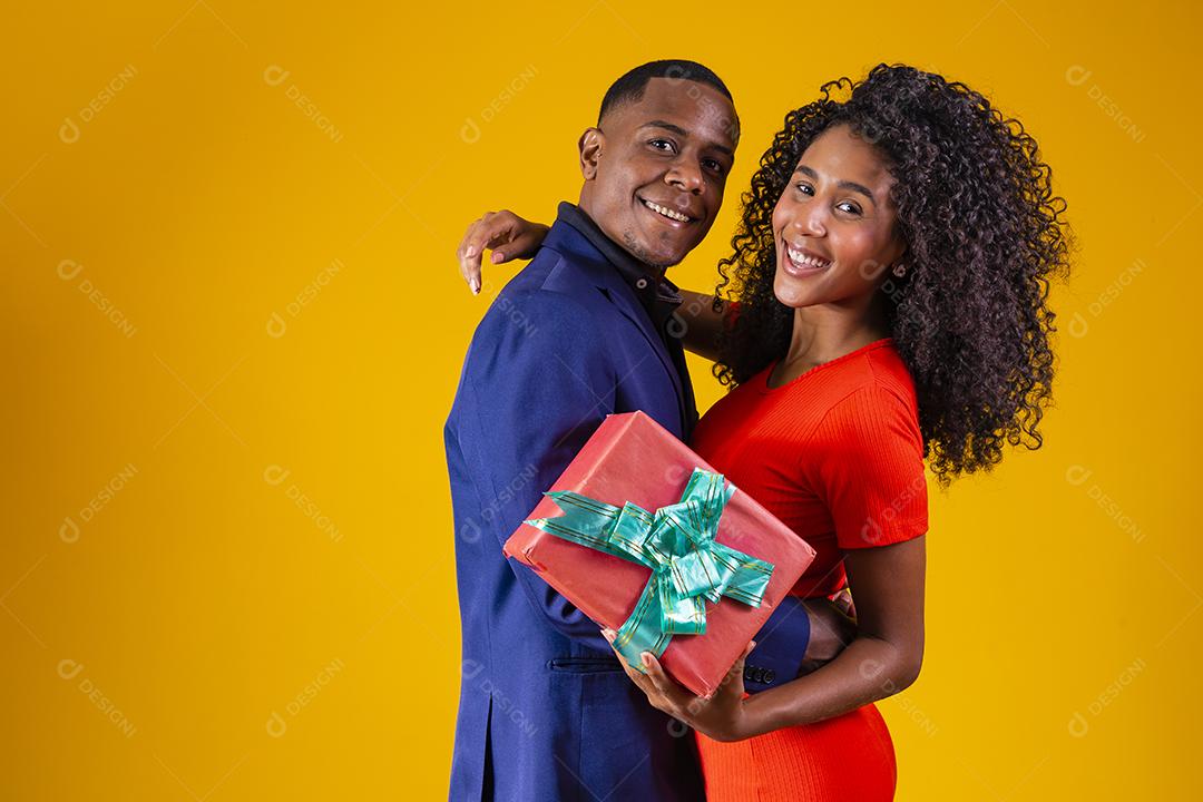 Retrato de um lindo casal afro em fundo amarelo segurando um presente