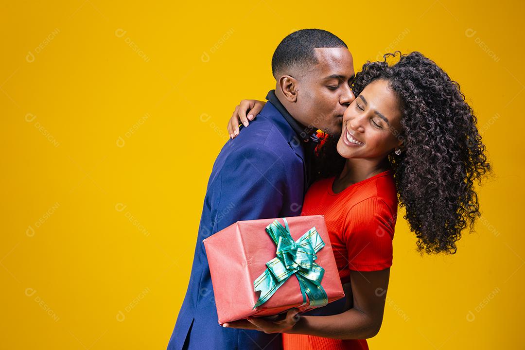 Retrato de um lindo casal afro em fundo amarelo segurando um presente