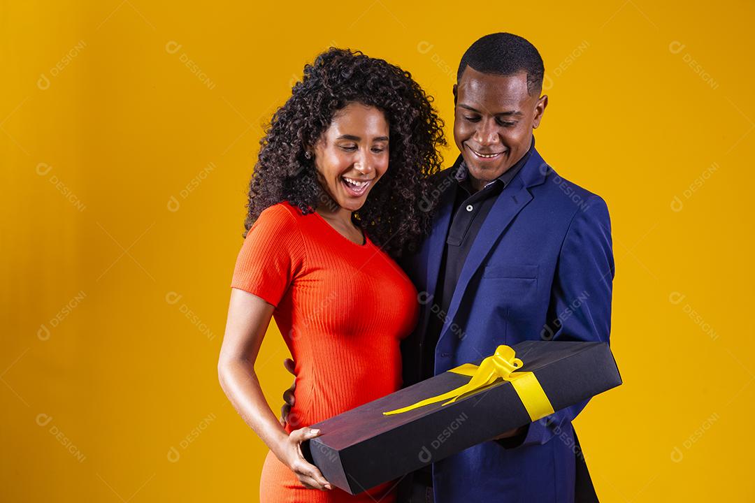 Retrato de um lindo casal afro em fundo amarelo segurando um presente