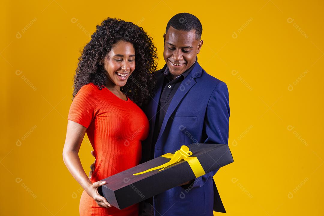 Retrato de um lindo casal afro em fundo amarelo segurando um presente