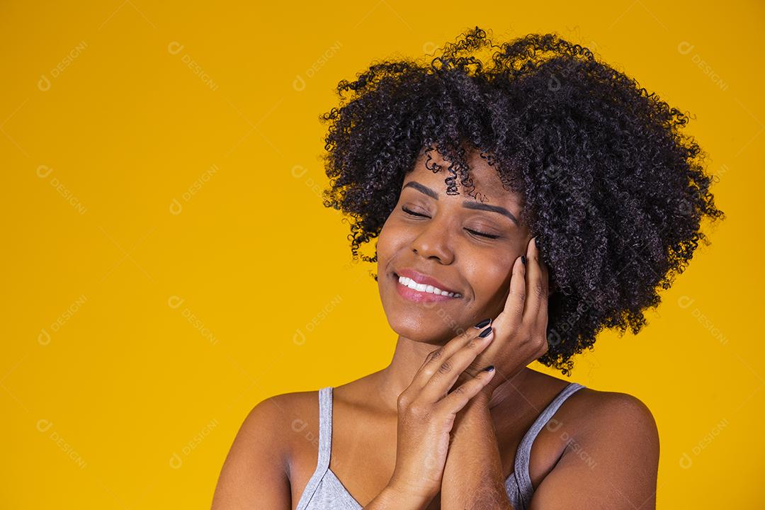 Retrato da beleza da menina afro com pele limpa e saudável em fundo amarelo. Sorrindo sonhadora