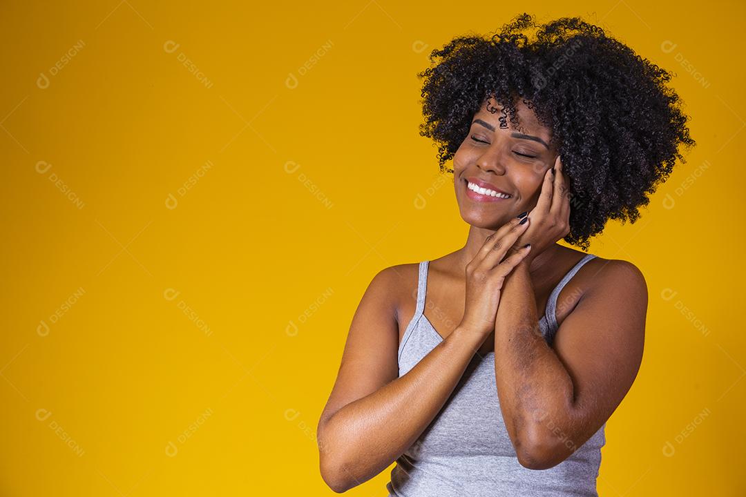 Retrato da beleza da menina afro com pele limpa e saudável em fundo amarelo. Sorrindo sonhadora