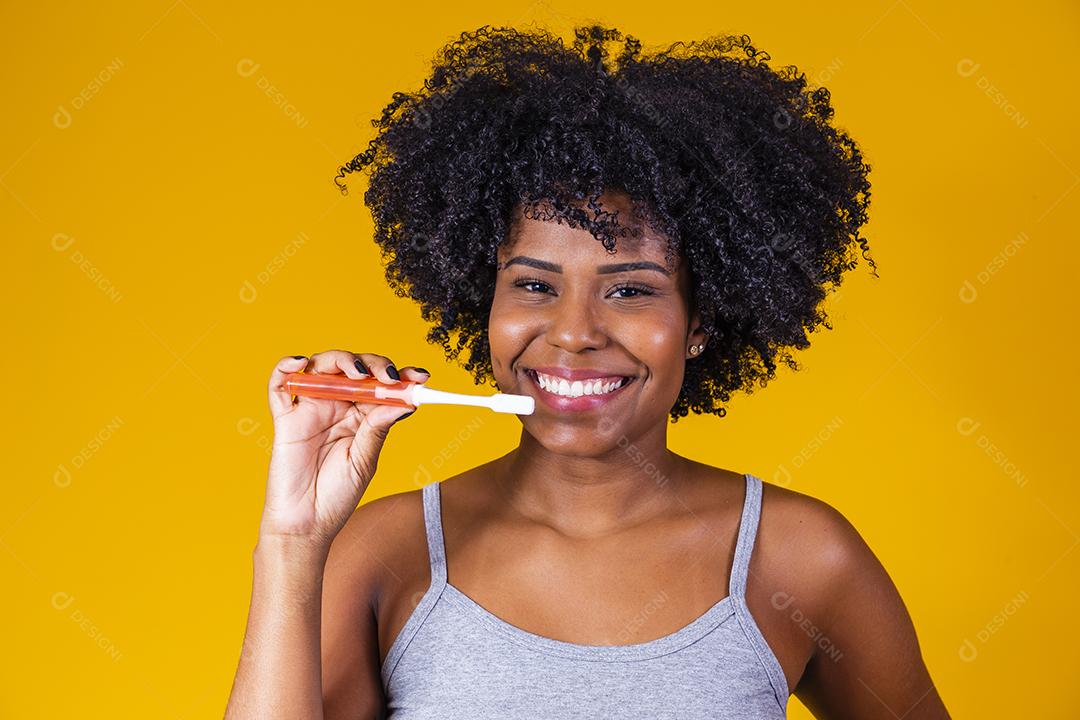Jovem afro escovando os dentes com uma escova de dentes