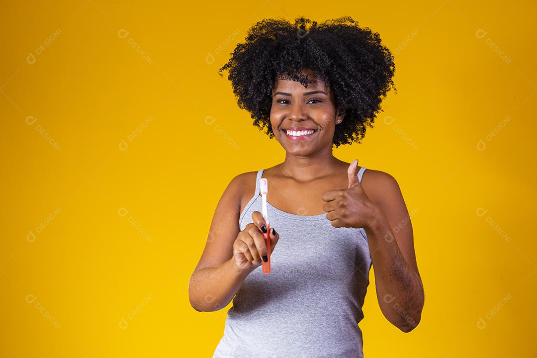 Jovem afro segurando uma escova de dentes em fundo amarelo. saúde bucal