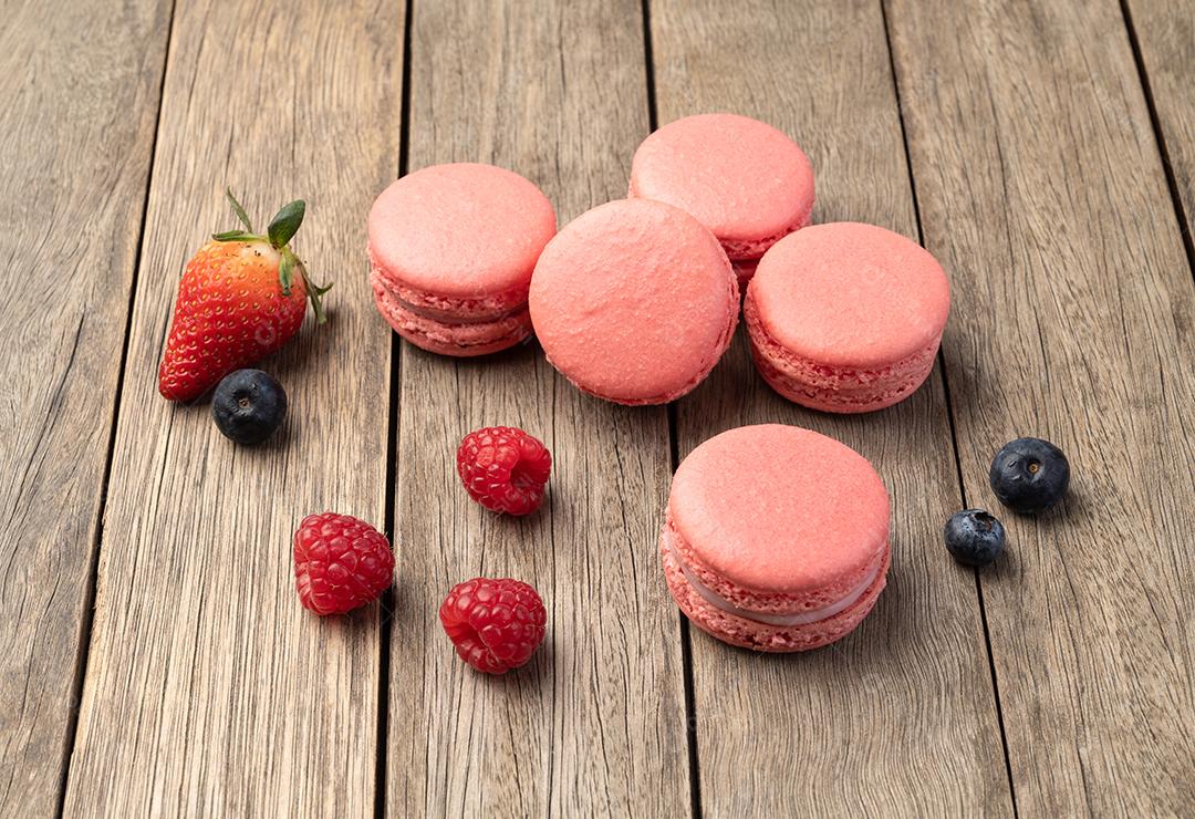 Macarons de Berry com morangos, framboesas e mirtilos sobre a mesa de madeira.