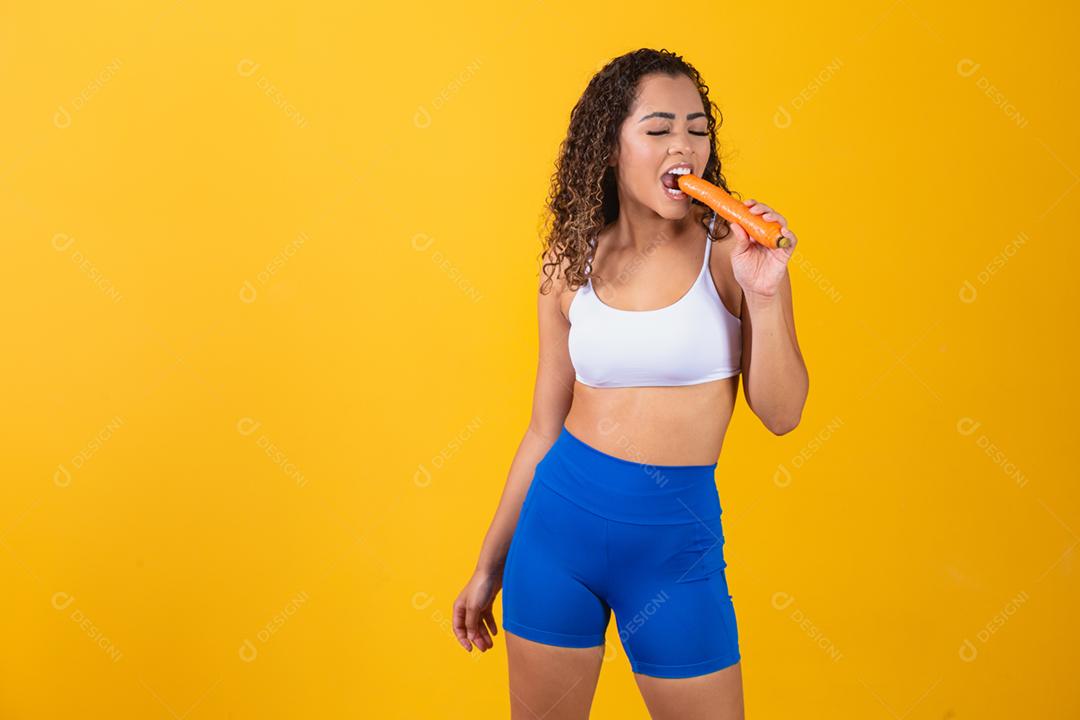 Mulher sorridente morde cenoura. Retrato de estúdio isolado