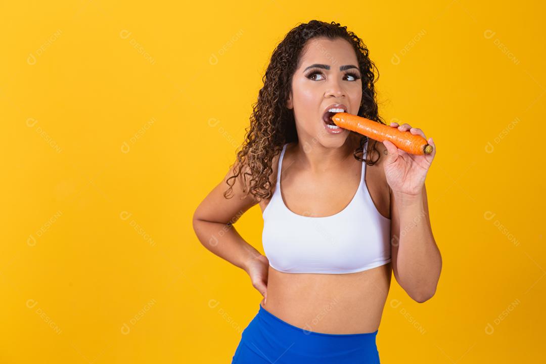 Mulher sorridente morde cenoura. Retrato de estúdio isolado