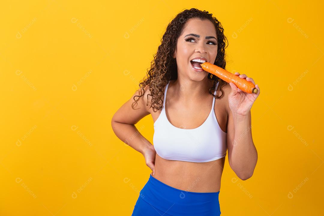 Mulher sorridente morde cenoura. Retrato de estúdio isolado