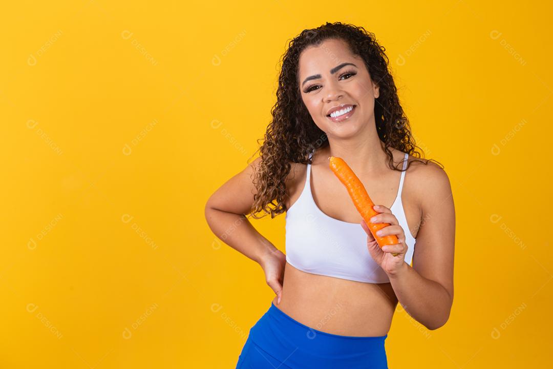 Mulher sorridente morde cenoura. Retrato de estúdio isolado