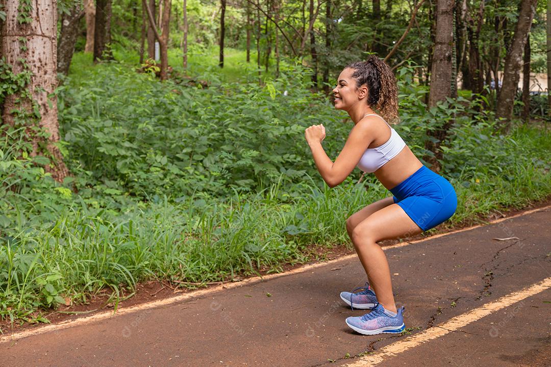 Desportiva mulher afro-americana treinando no parque. Mulher fazendo agachamento no parque.