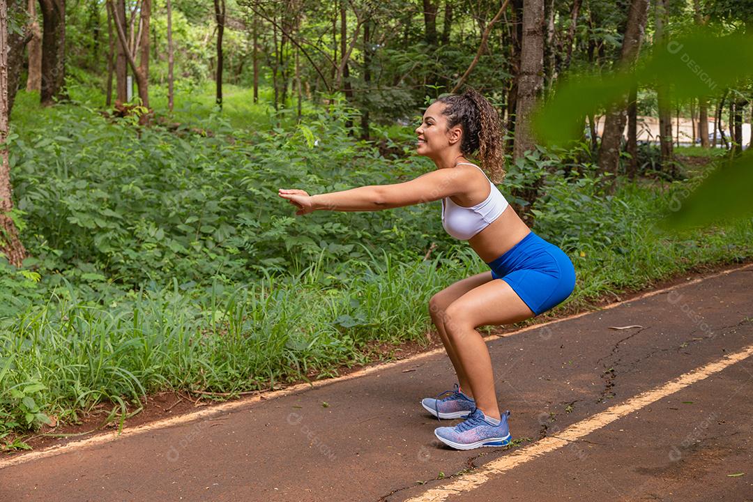 Desportiva mulher afro-americana treinando no parque. Mulher fazendo agachamento no parque.