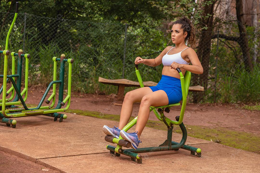 Jovem se exercitando no parque. Jovem mulher fazendo exercícios de musculação no peito e nas costas.