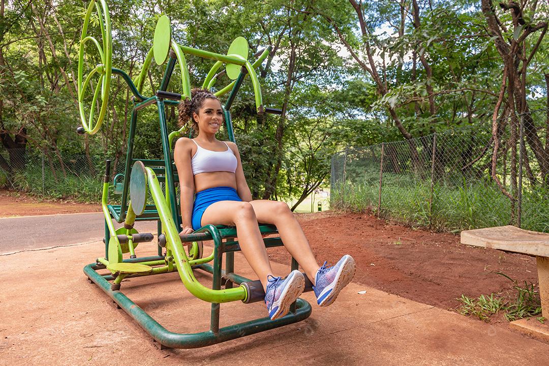 Jovem se exercitando no parque. Jovem mulher fazendo exercício de perna no exercitador de pernas.