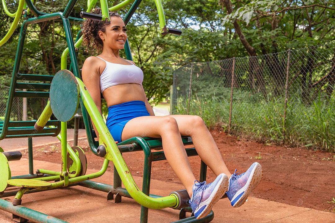 Jovem se exercitando no parque. Jovem mulher fazendo exercício de perna no exercitador de pernas.