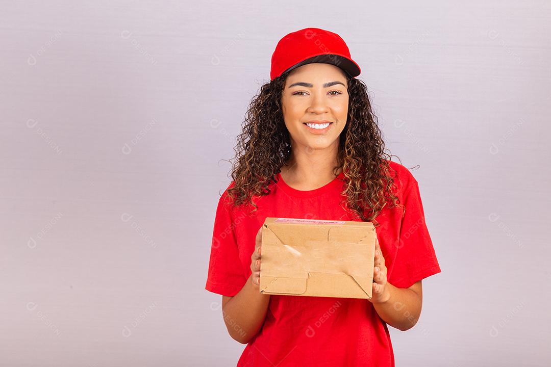 Linda jovem mensageiro entregando um pacote. Uma entregadora de uniforme vermelho está sorrindo
