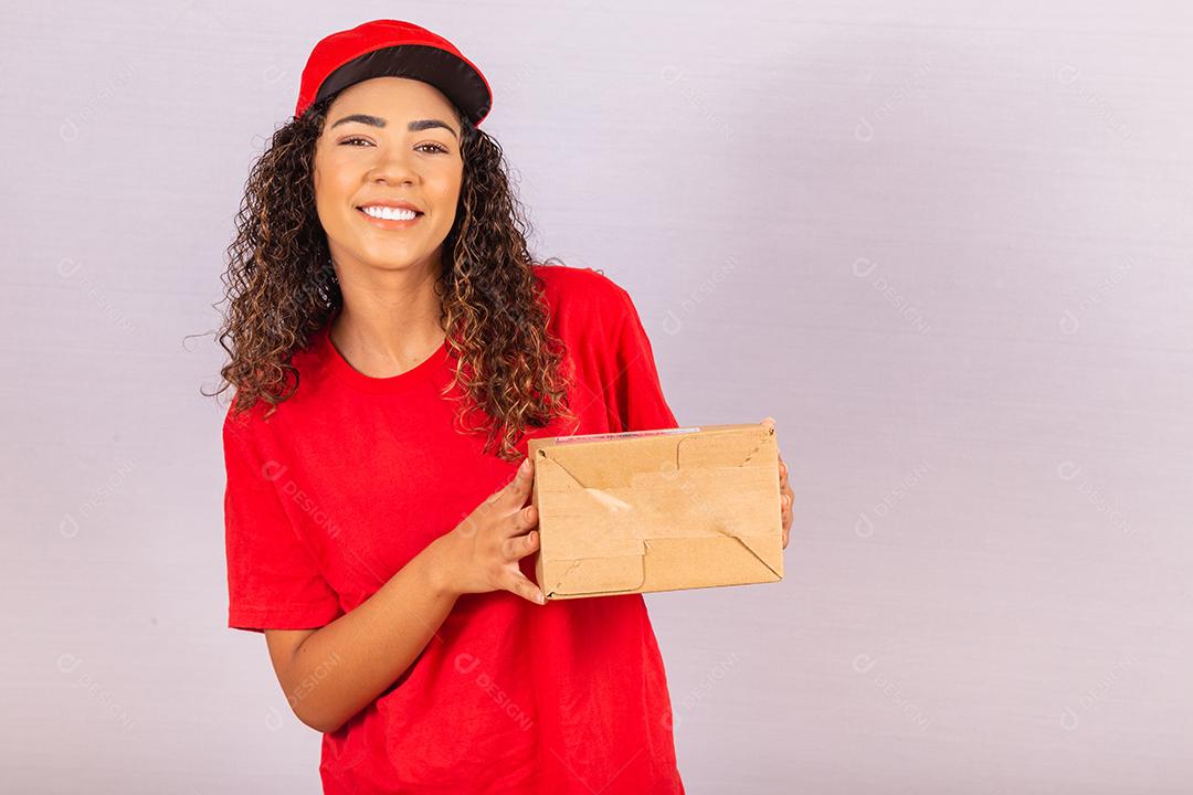 Linda jovem mensageiro entregando um pacote. Uma entregadora de uniforme vermelho está sorrindo