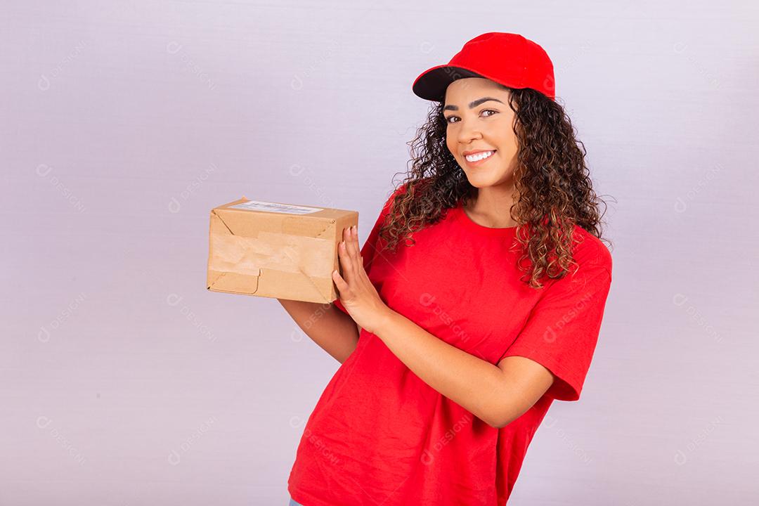 Linda jovem mensageiro entregando um pacote. Uma entregadora de uniforme vermelho está sorrindo