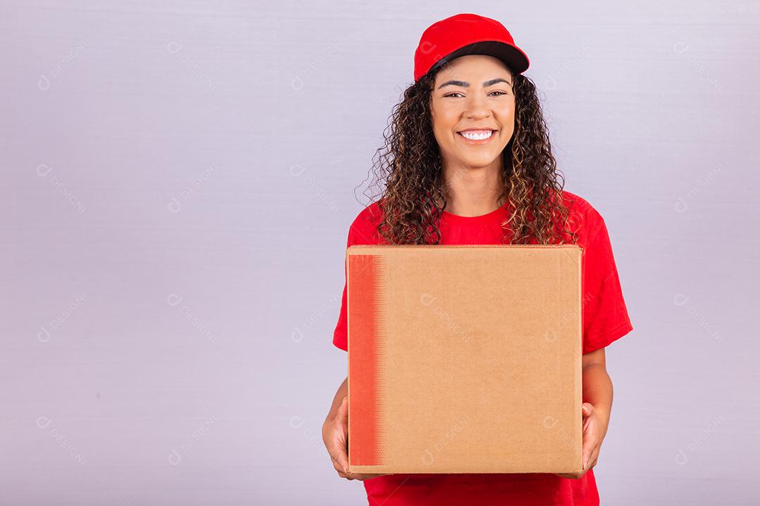 Linda jovem mensageiro entregando um pacote enorme. Uma entregadora de uniforme vermelho está sorrindo