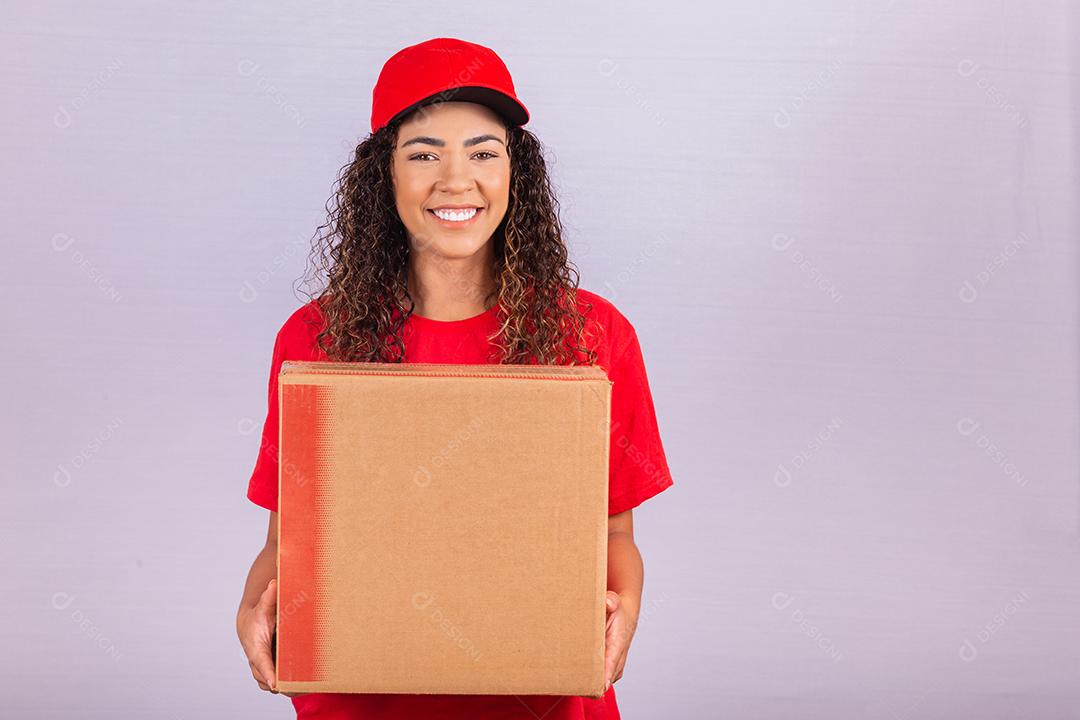 Linda jovem mensageiro entregando um pacote enorme. Uma entregadora de uniforme vermelho está sorrindo