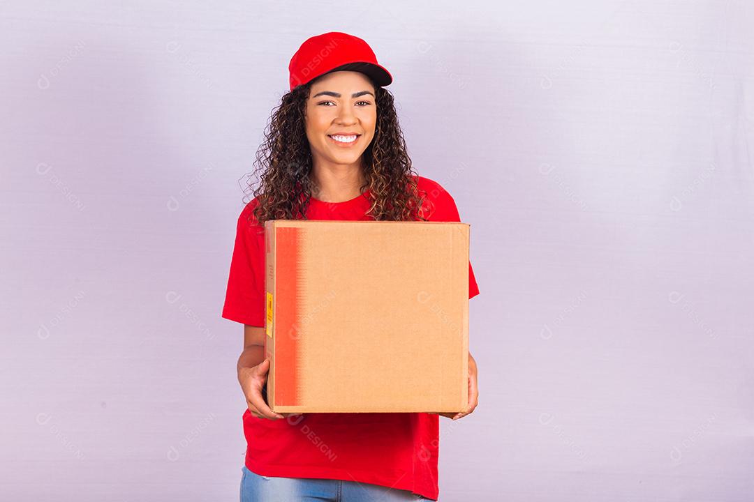 Linda jovem mensageiro entregando um pacote enorme. Uma entregadora de uniforme vermelho está sorrindo